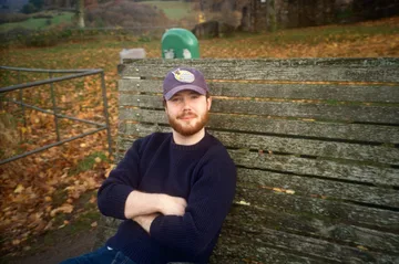Joris on a wooden bench in autumn leaves, arms crossed